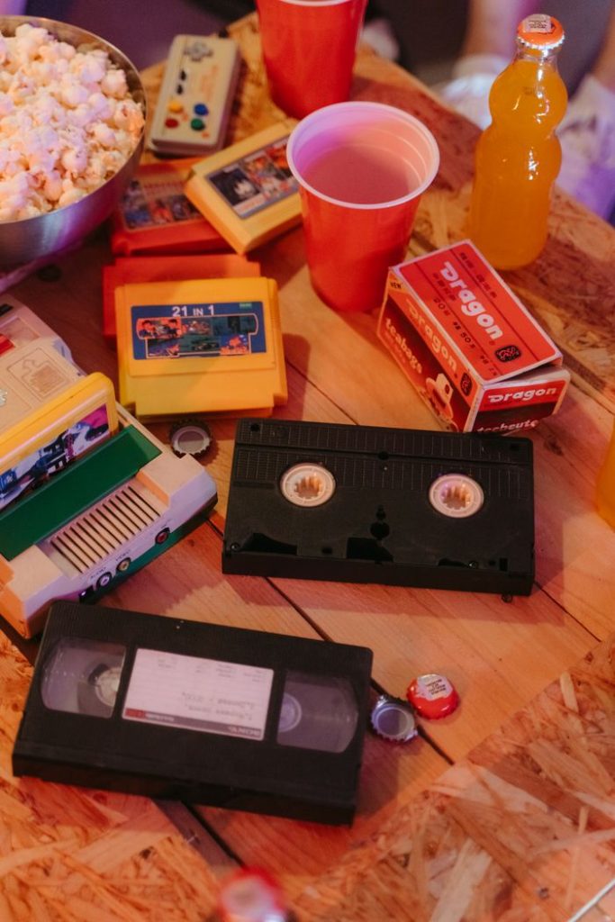 A vintage-themed table setup featuring VHS tapes, popcorn, and retro drinks.